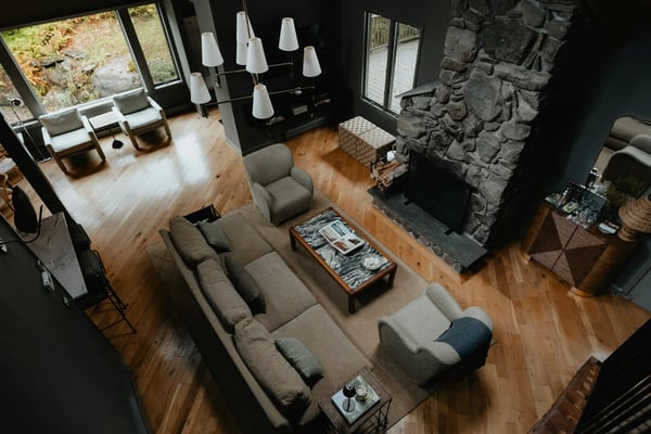 Open-plan living room with gray sectional sofa, stone fireplace, wooden floors, and skylights overlooking trees