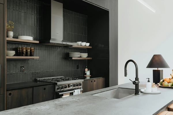Modern kitchen with dark tile backsplash, gas range, floating wood shelves, marble countertop, and black faucet