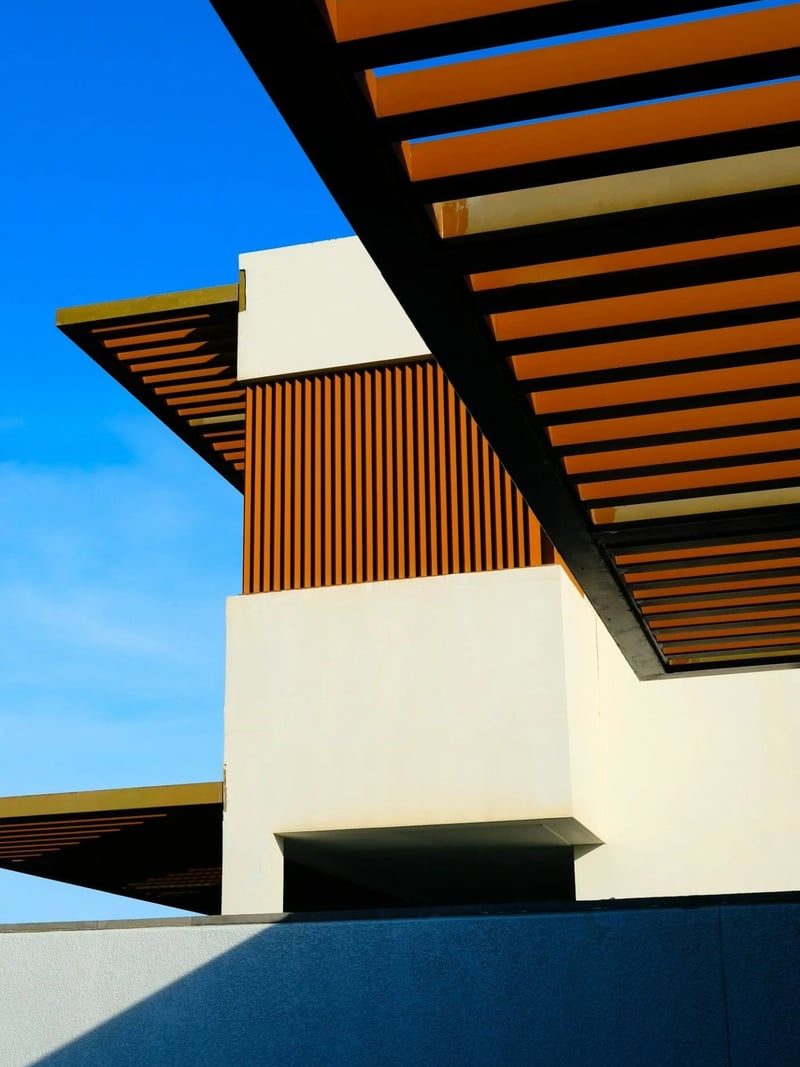 Modern white building with orange and black wooden slat overhangs against clear blue sky