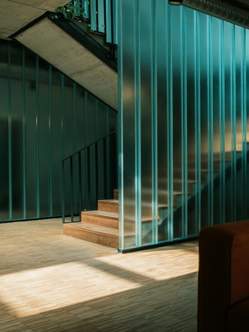 Modern interior with teal glass partition walls, wooden stairs, and concrete ceiling with metal ductwork