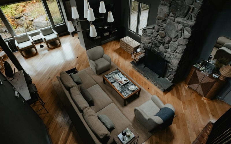 Open-plan living room with gray sectional sofa, stone fireplace, wood floors, and skylights overlooking greenery